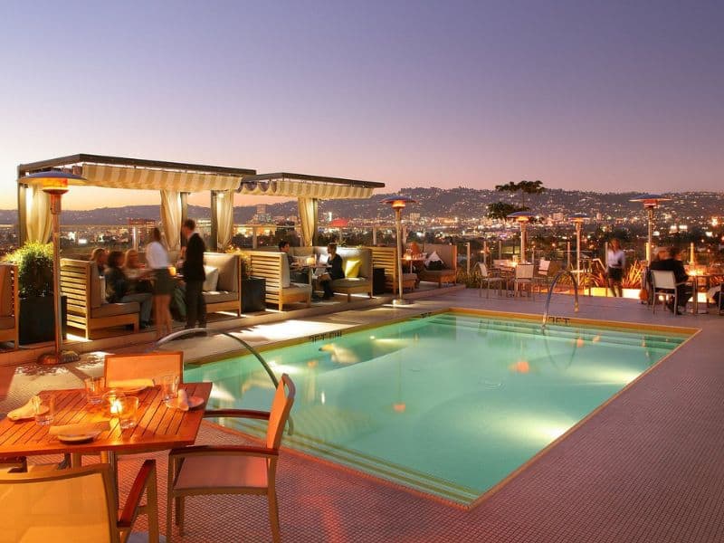 Rooftop pool area of Kimpton The Hotel Wilshire in Los Angeles at dusk with guests socializing and city lights in the background.