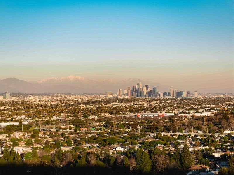 View of the Los Angeles skyline with visible skyscrapers against the backdrop of the San Gabriel Mountains, as seen from the Baldwin Hills Scenic Overlook Trail.