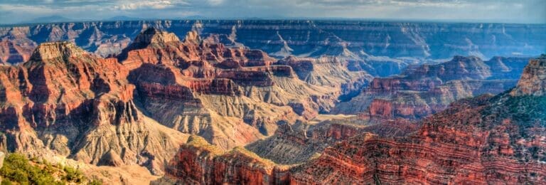 Panoramic view of the Grand Canyon showcasing its vast array of red rock formations and canyons, captured during the day with shadows accentuating the rugged terrain.