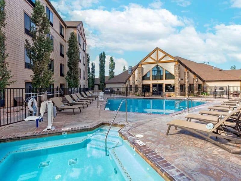 Outdoor pool and hot tub area at the Best Western Plus Bryce Canyon Grand Hotel, with lounge chairs and poolside amenities. The hotel's multi-story structure and central lodge with large windows are visible in the background.