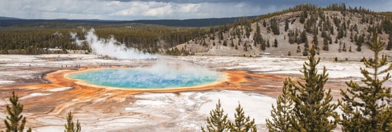 Overcast sky above Grand Prismatic Spring in Yellowstone National Park, showcasing the spring's striking colors and steam amidst the landscape.