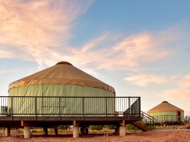 Two Wingate Yurts at Dead Horse Point State Park with wooden decks and railings, set against a backdrop of a clear sky with soft, pink clouds at sunset. Photo Credit: CRSA