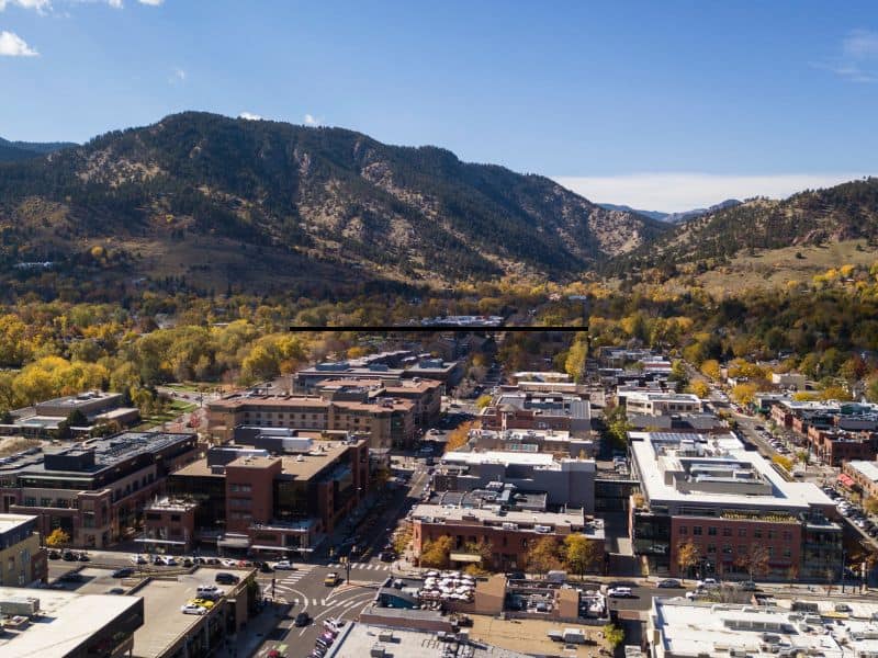 Aerial view of Boulder, Colorado, showing the city buildings and streets with a backdrop of the surrounding mountains and fall foliage.