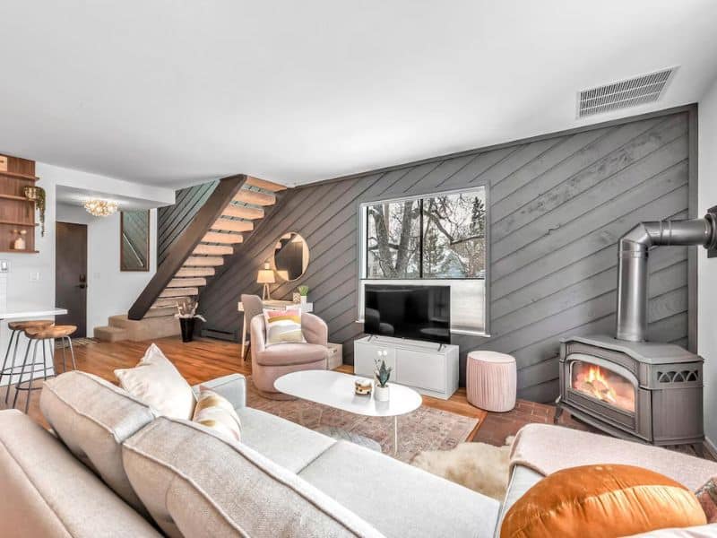 Living room of a Vrbo rental in Boulder, Colorado, featuring a sectional sofa, a round coffee table, a TV, a wood-burning stove, and a staircase with wooden steps.