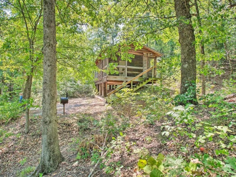 Exterior of Bright Davis Escape cabin rental near Turner Falls, set in a wooded area with a screened porch and a grill.