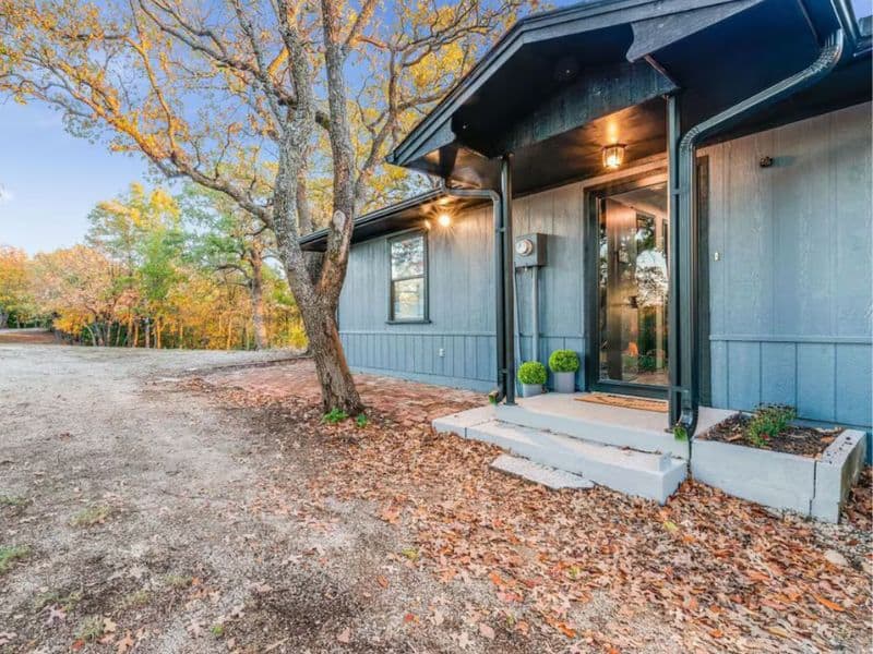 Exterior of Hickory Hill Hideaway cabin near Turner Falls with a dark gray facade, a small front porch, and surrounding autumn trees.