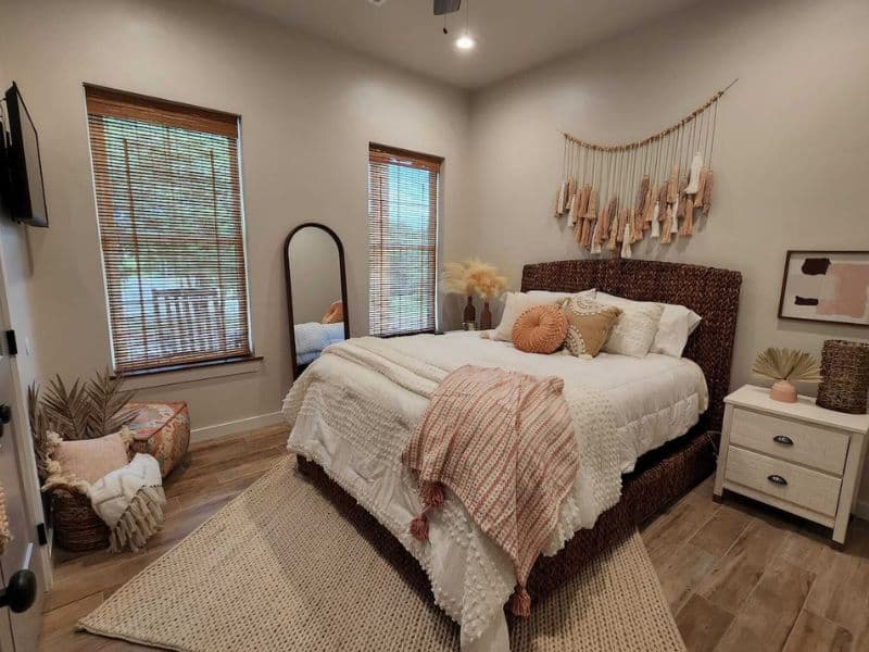 Bedroom inside the Lake Escape Vrbo cabin rental near Turner Falls featuring a bed with a woven headboard, decorative pillows, a cozy blanket, and natural light from two windows with bamboo blinds.