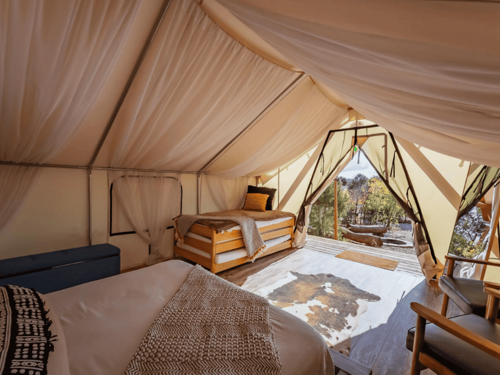 Interior of a glamping tent at Zion Ponderosa Ranch Resort, furnished with comfortable beds, cozy linens, and a cowhide rug, with the tent flaps open to a scenic view.