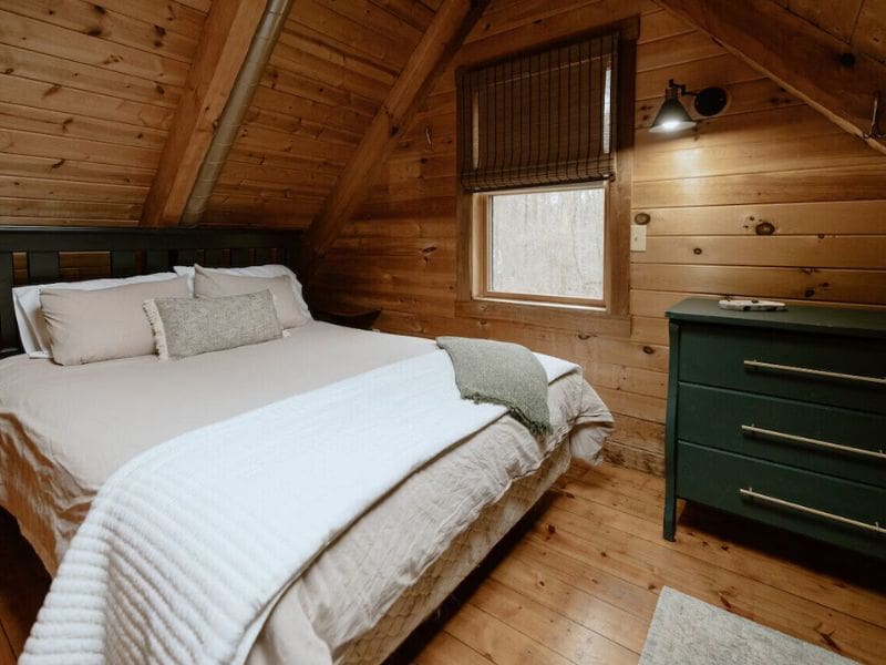 A snug loft bedroom with wooden ceilings, a comfortable bed dressed in white linens, and a simple green dresser.